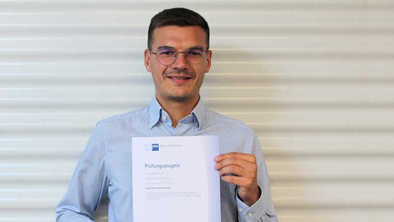 Hannes Büscherhoff mit Prüfungszeugnis in der Hand steht vor Wellblechprofil in weiß