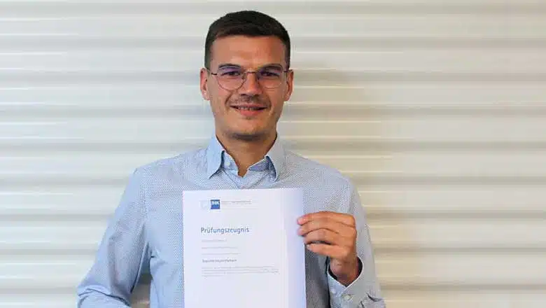 Hannes Büscherhoff mit Prüfungszeugnis in der Hand steht vor Wellblechprofil in weiß